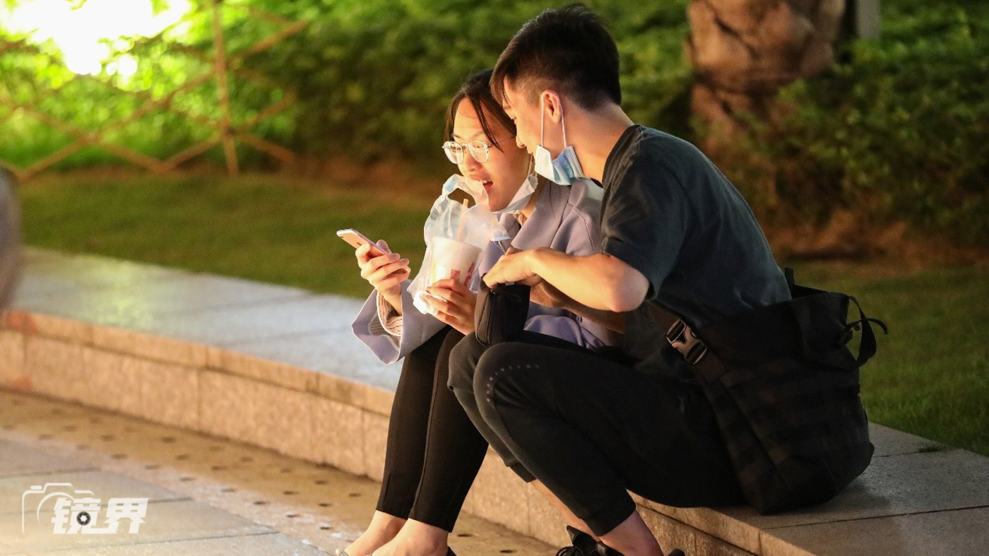 公园的寂静一角,一对情侣坐在台阶上休息,用手机刷着搞笑短视频.